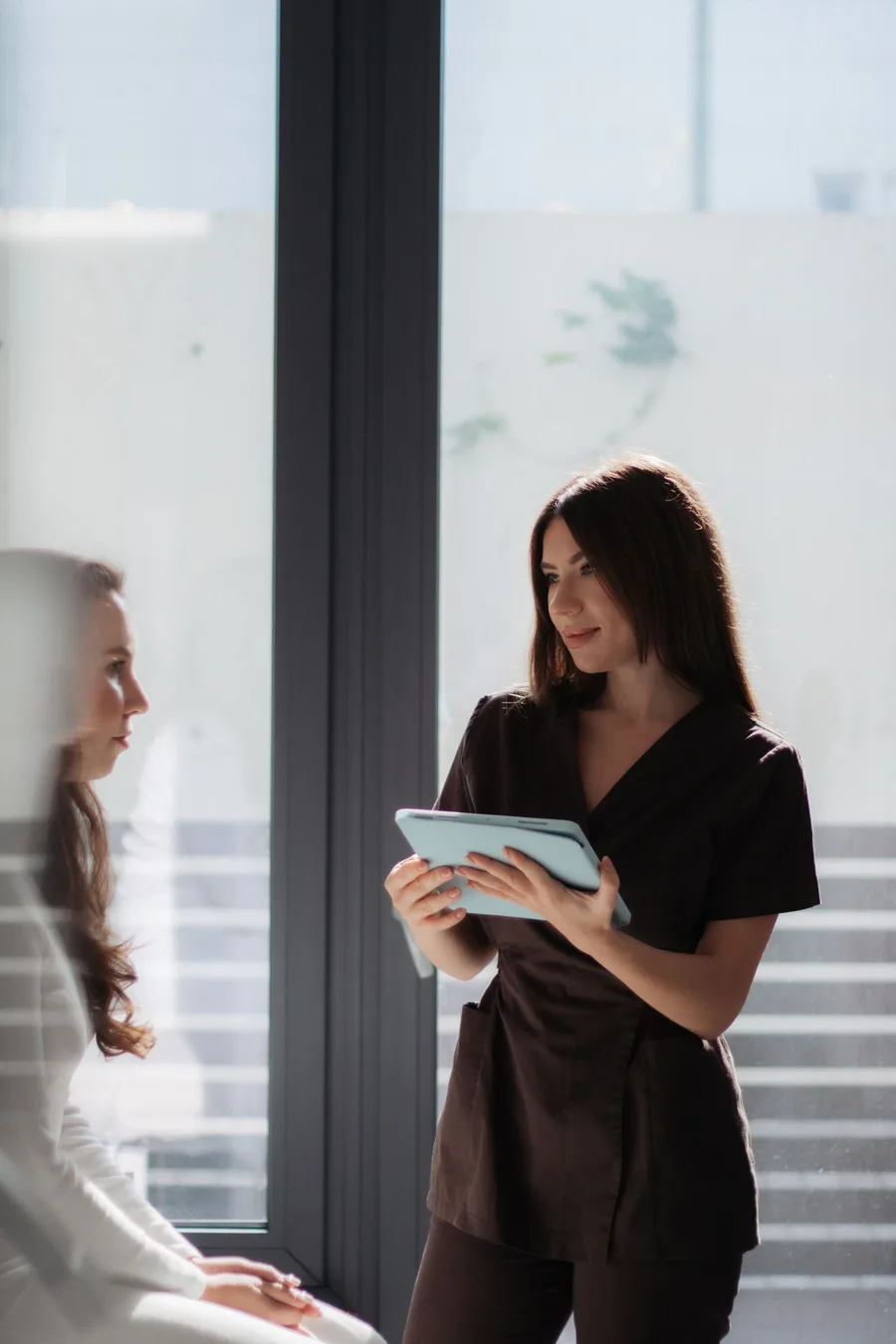 A clinician showing a tablet to a patient beside a window in a consultation room